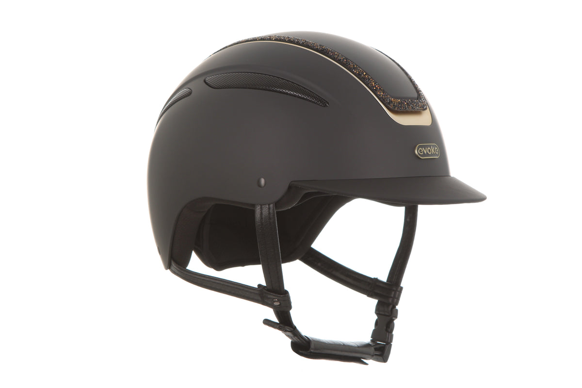 A matte black equestrian riding helmet with a small gold logo on the side and a subtle gold glittery decorative stripe on the top, shown against a plain white background.